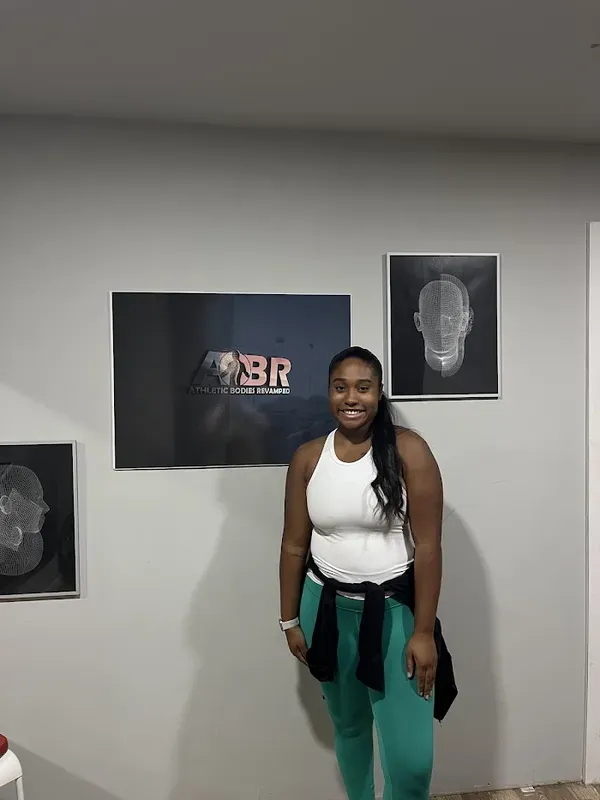 Maya Sharpe smiling beside the Athletic Bodies Revamped sign in her studio